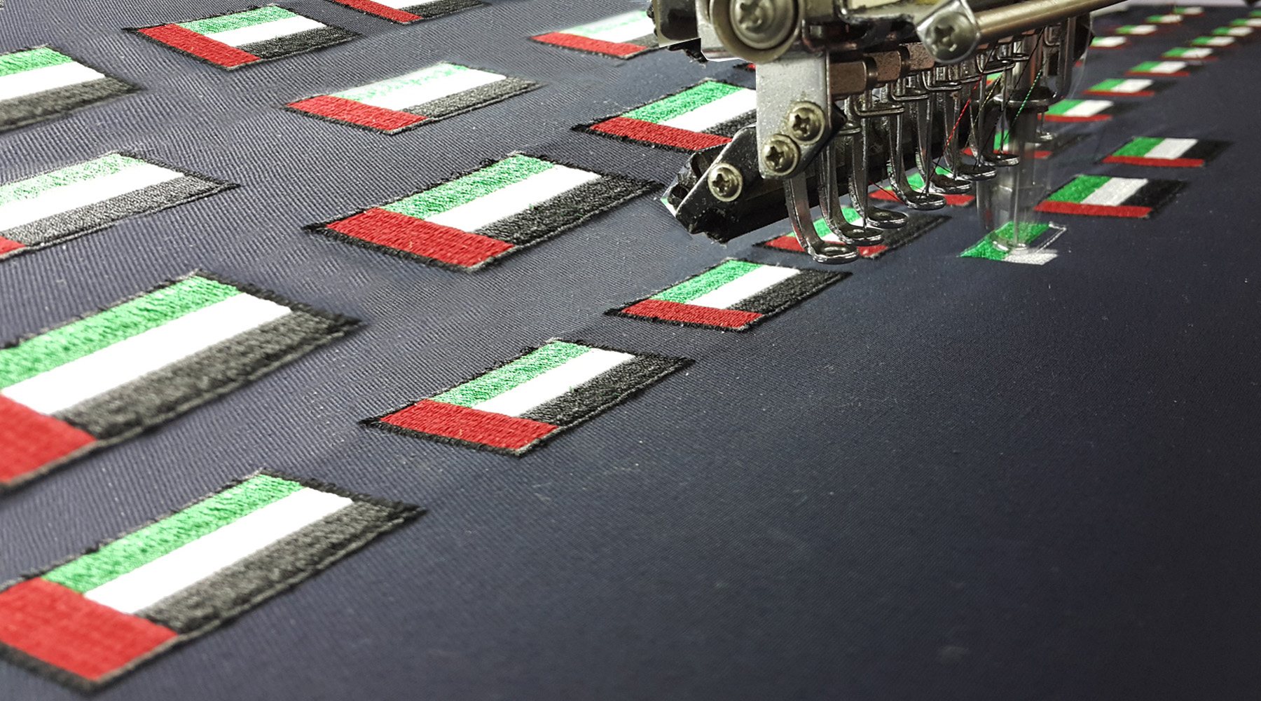 Multi-head embroidery machine stitching rows of UAE-flag patches on dark fabric