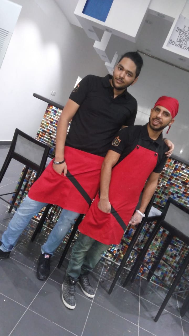 Two restaurant staff in black T-shirts and red waist-to-knee aprons