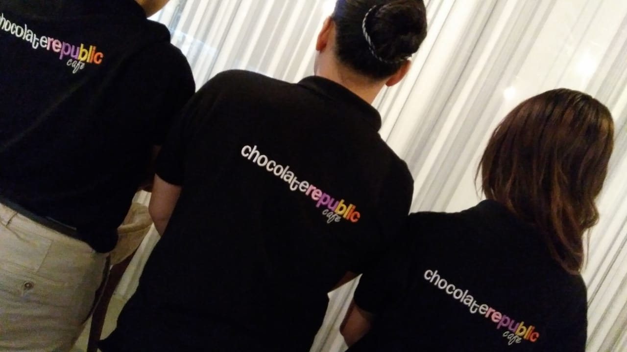 Staff seen from behind wearing black T-shirts with a printed brand name across the back