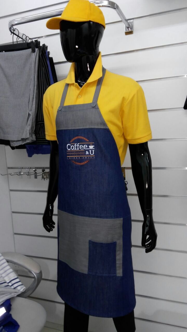 Navy denim bib apron with grey pocket panel over a yellow polo and yellow cap on a mannequin
