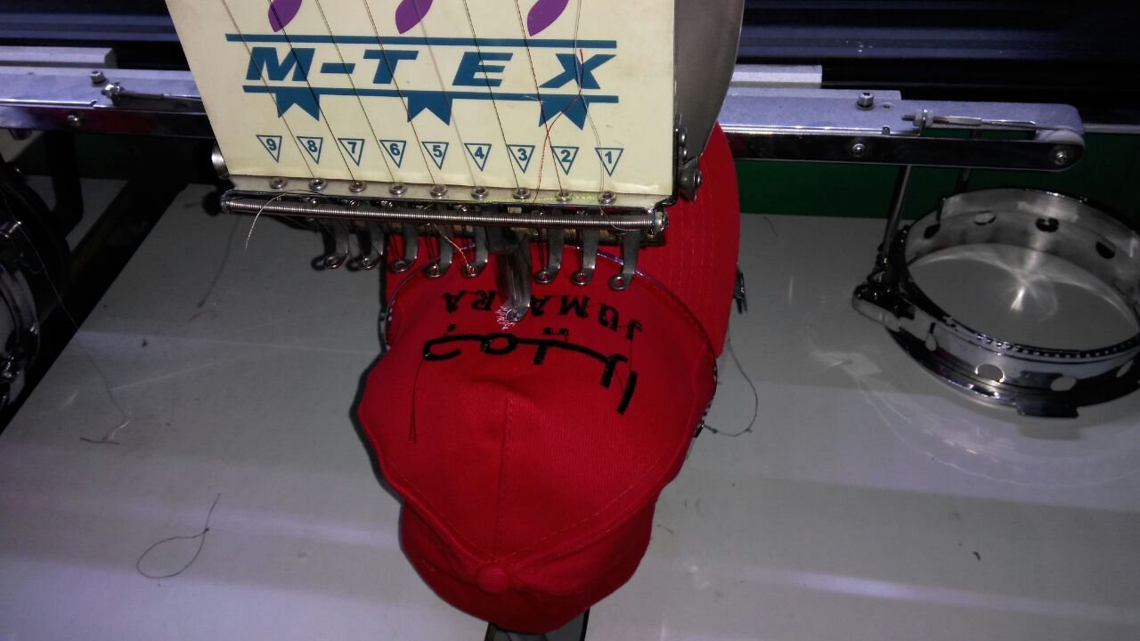 Single-head M-TEX embroidery machine stitching Arabic lettering onto a red cap