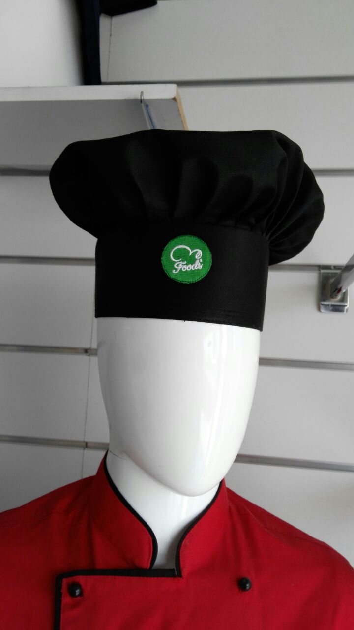 Black pleated chef hat with an embroidered green logo, worn with a red chef jacket on a mannequin