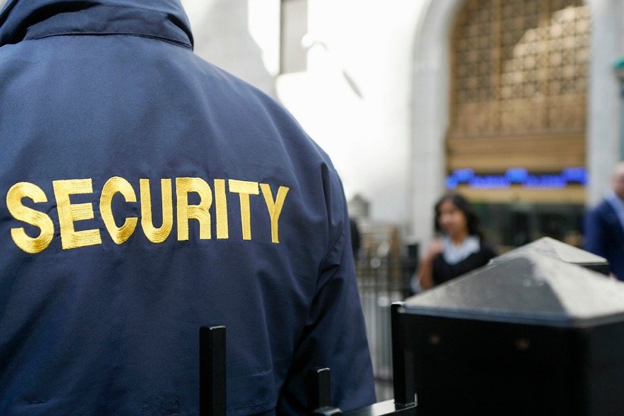 Security officer seen from behind in a navy jacket with yellow 'SECURITY' lettering