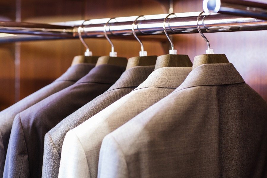 Row of suit jackets in beige and grey on wooden hangers